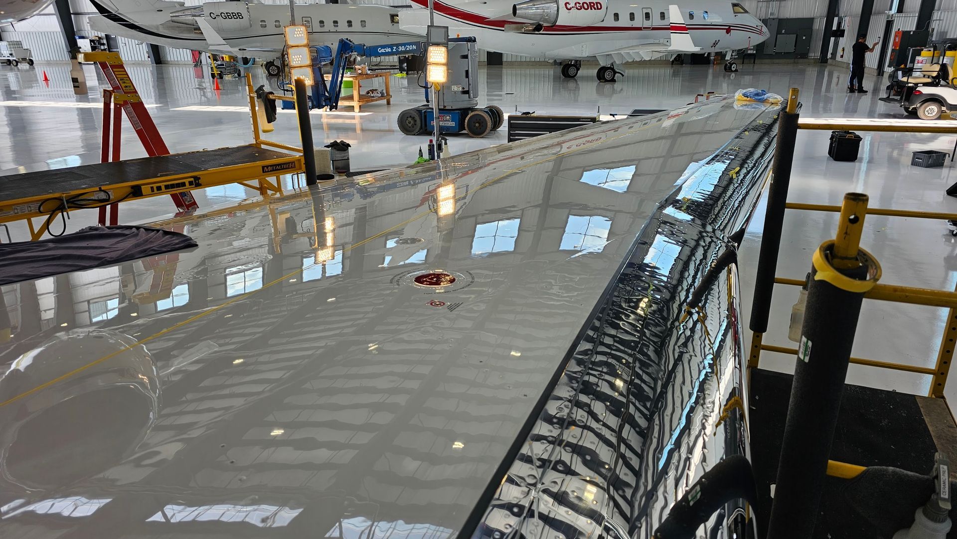 Aircraft wing, highly polished, reflecting a hangar interior with other planes and equipment.