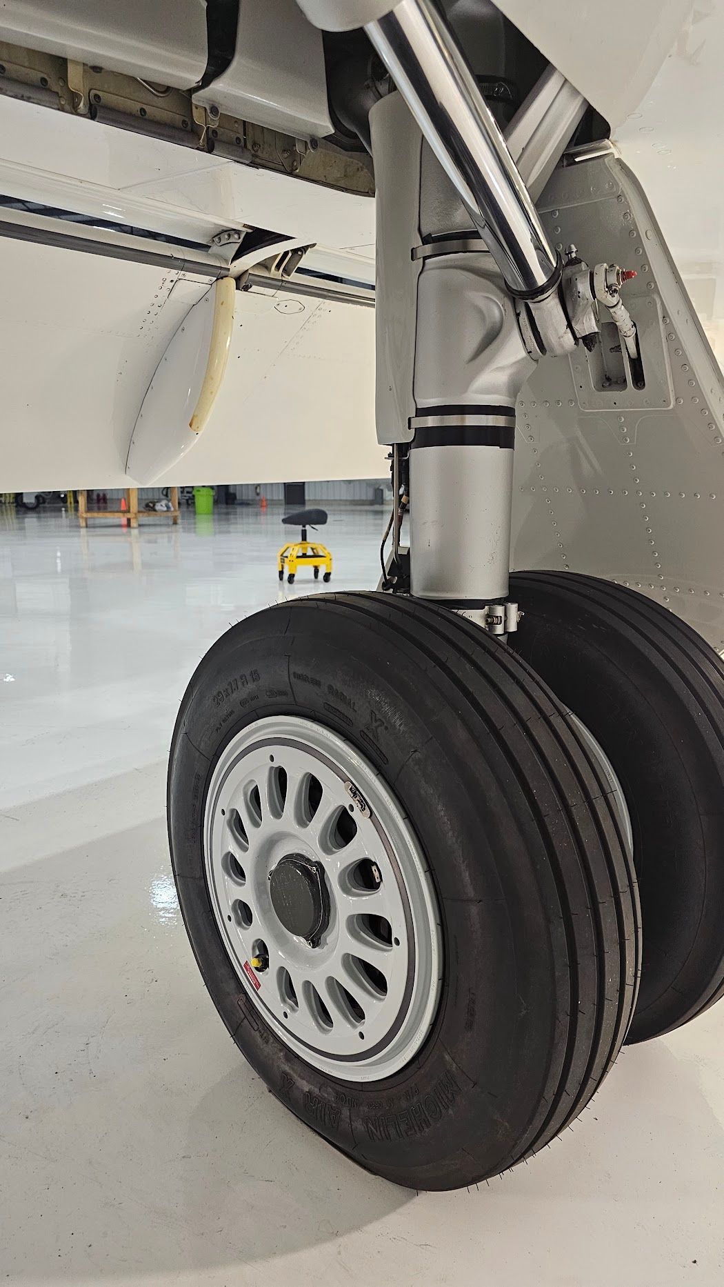 Aircraft landing gear with two tires on a silver rim, against a white fuselage.