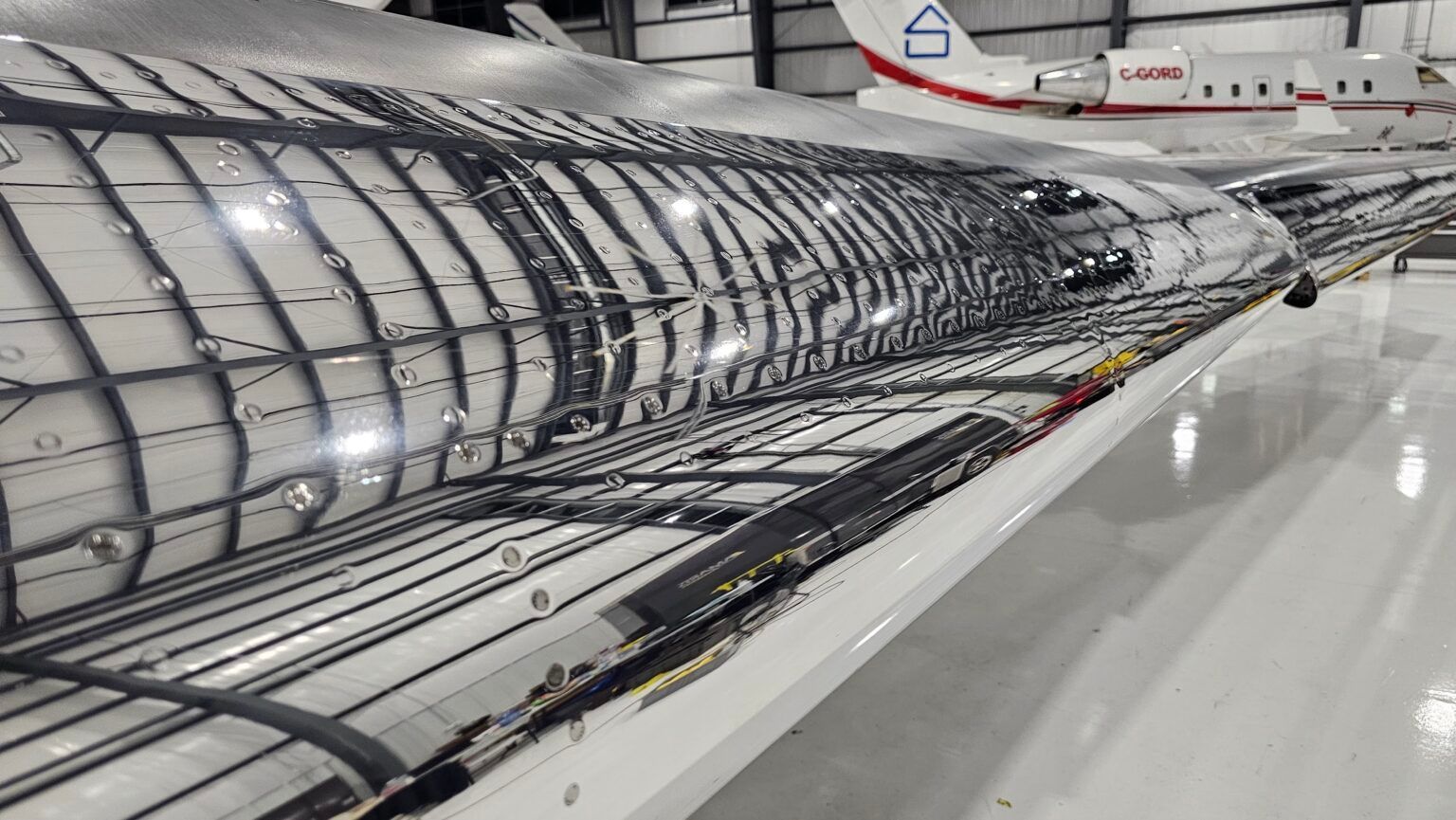 Close-up of a plane wing's internal structure, showing ribs and wiring. The reflective surface is silver.