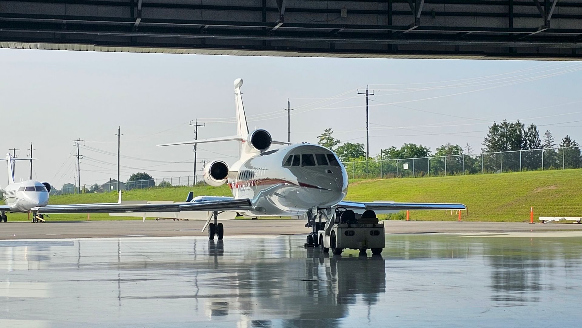 A private jet is on the tarmac. Silver and white fuselage, green grass, and blue sky.