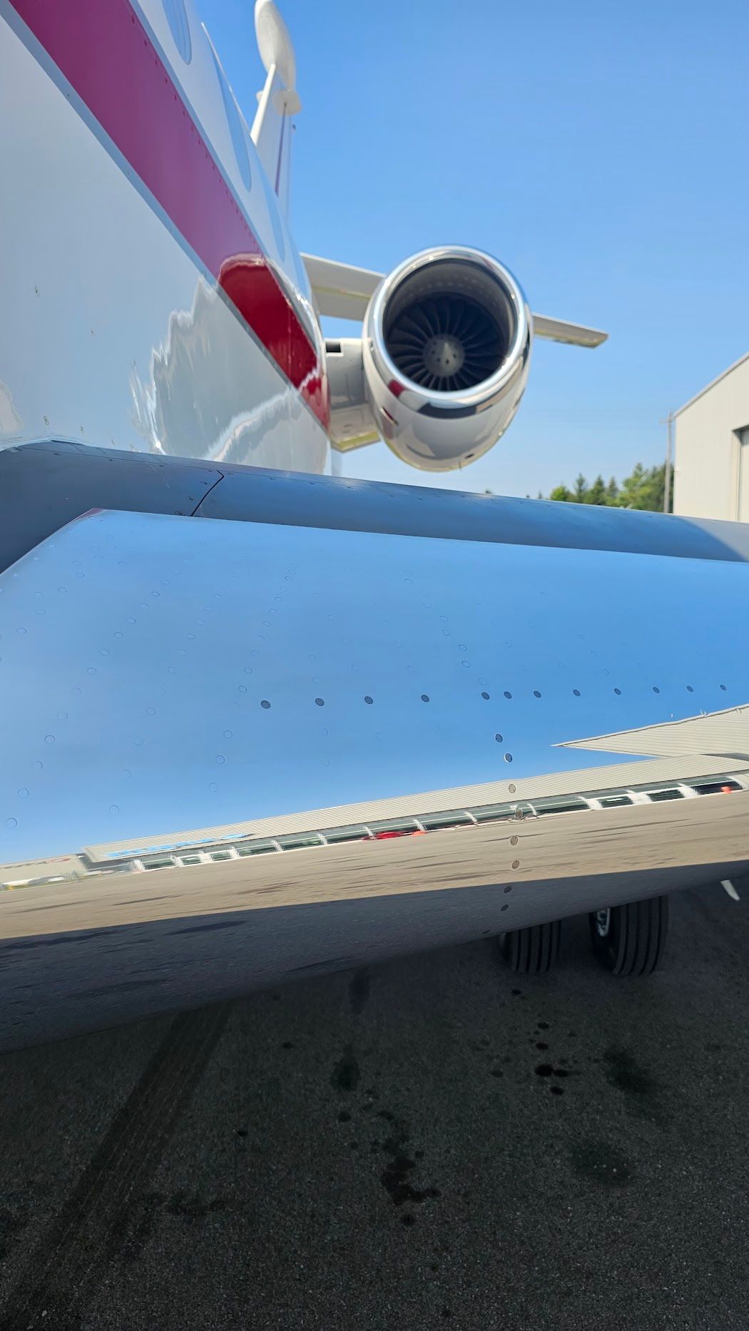 Jet engine and wing of a white private plane on the tarmac, against a blue sky.