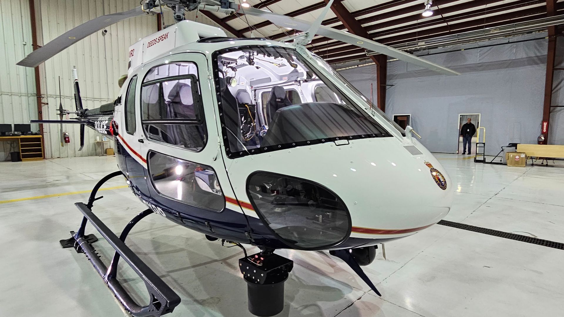 White and blue helicopter inside a hangar, parked on a concrete floor.