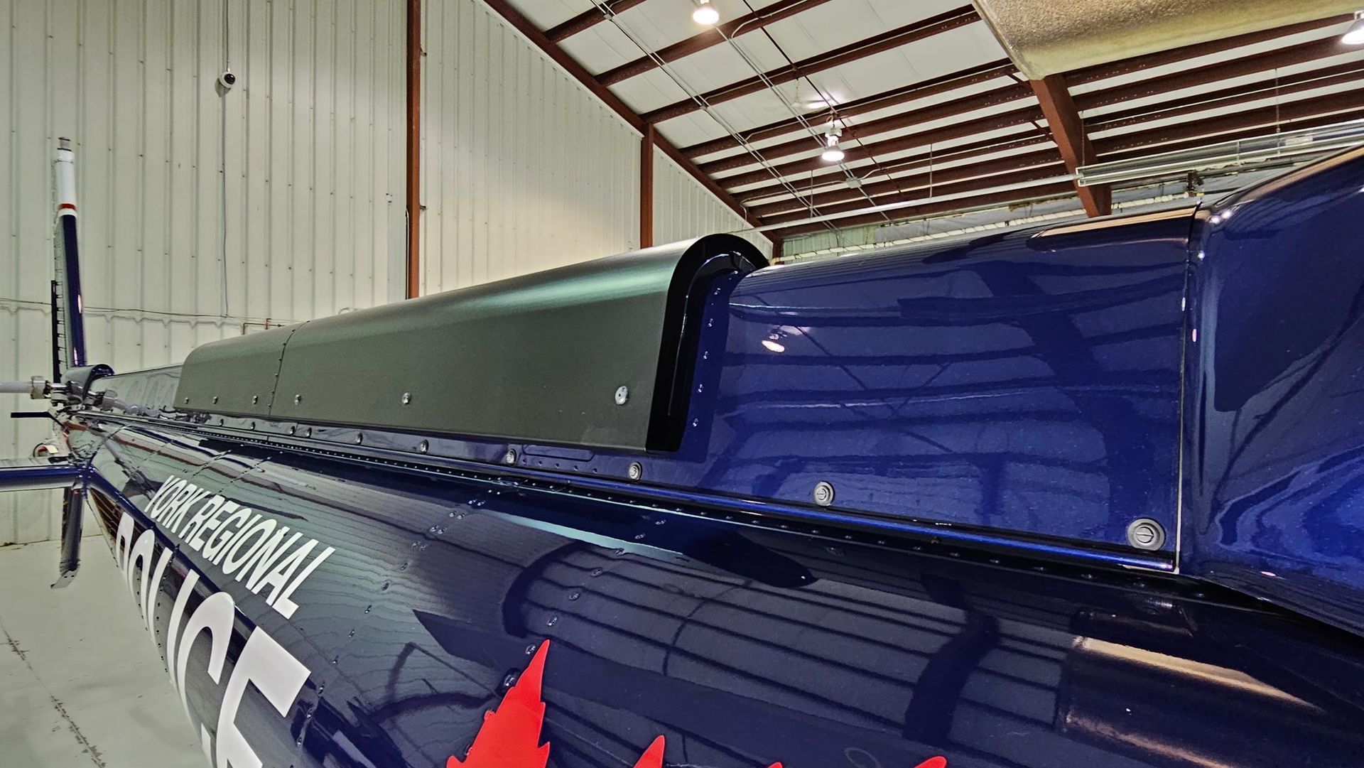 Blue helicopter fuselage with a dark grey cover, inside a hangar.