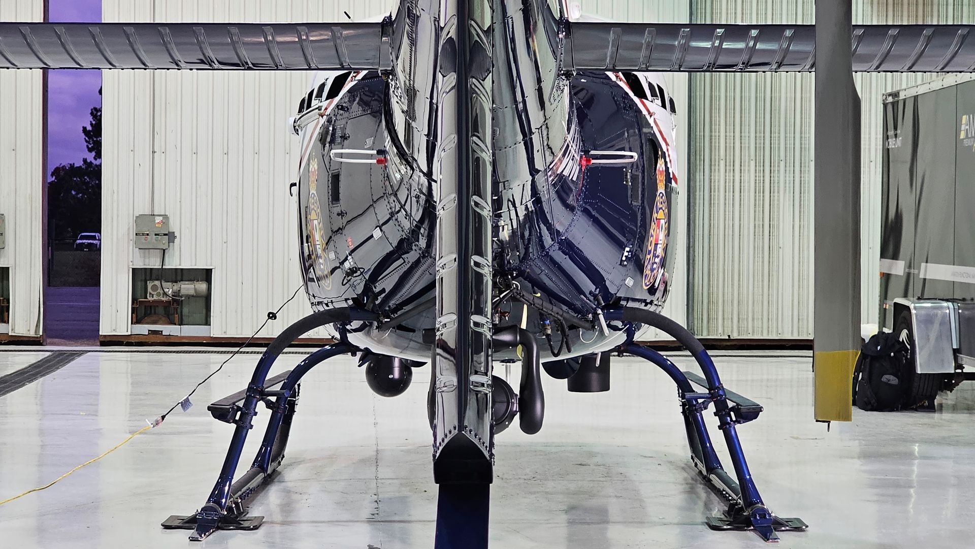 Rear view of a dark helicopter on landing gear inside a hangar.