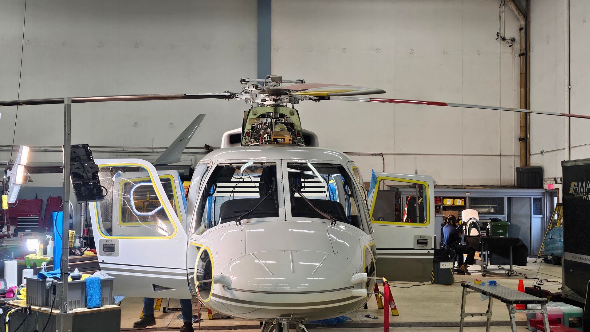 White helicopter in a hangar with open doors, undergoing maintenance.