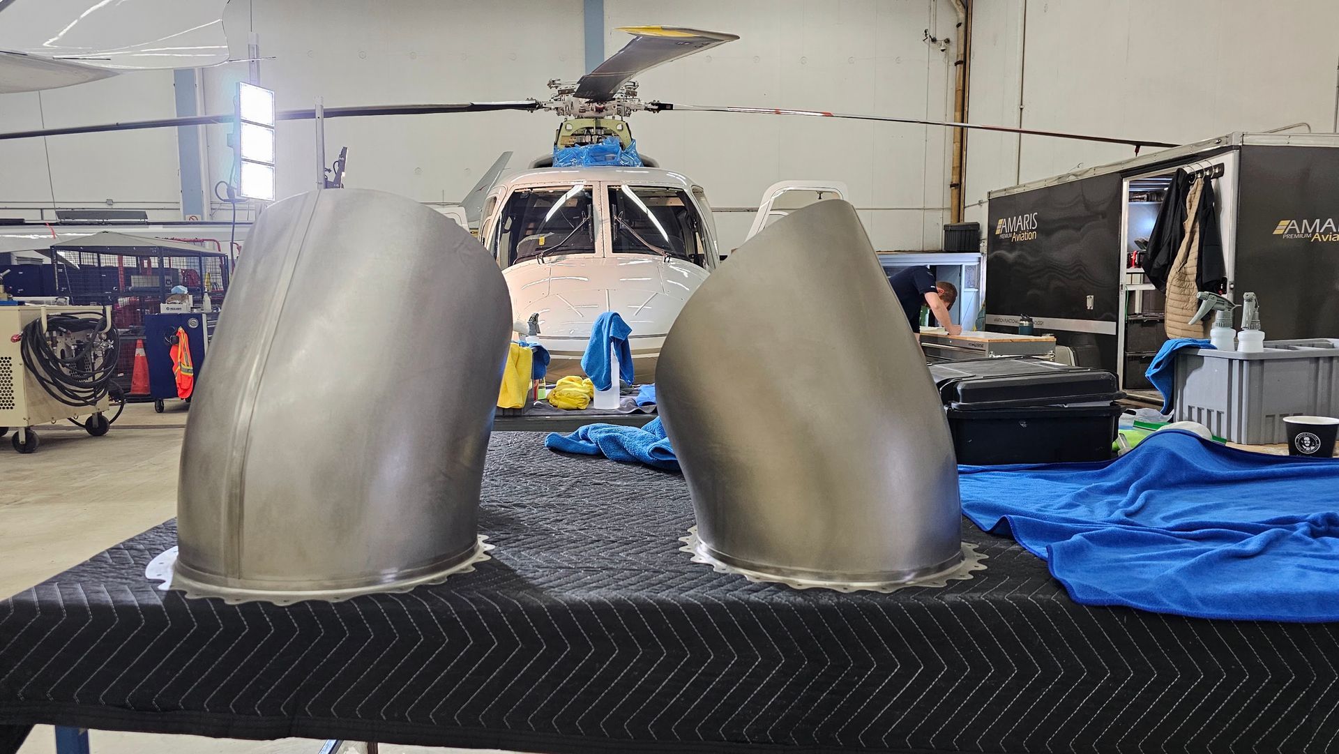 Two curved metal pieces sit in front of a helicopter in a hangar.