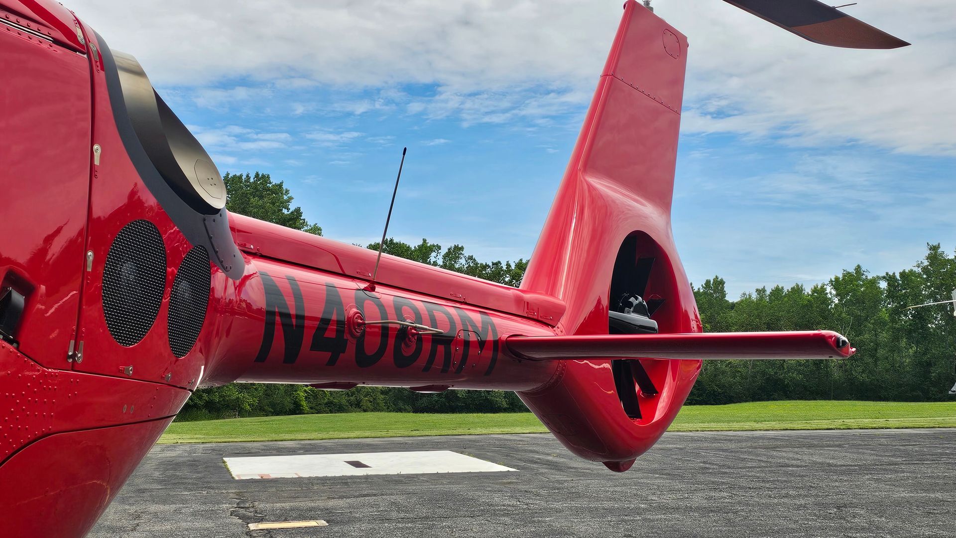 Red helicopter tail section with the tail rotor visible, parked on a tarmac.