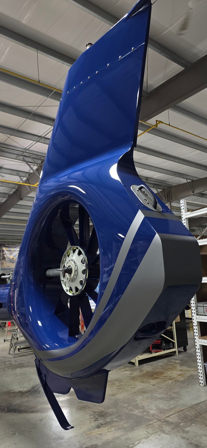 Blue and gray aircraft component with a fan, hanging indoors.