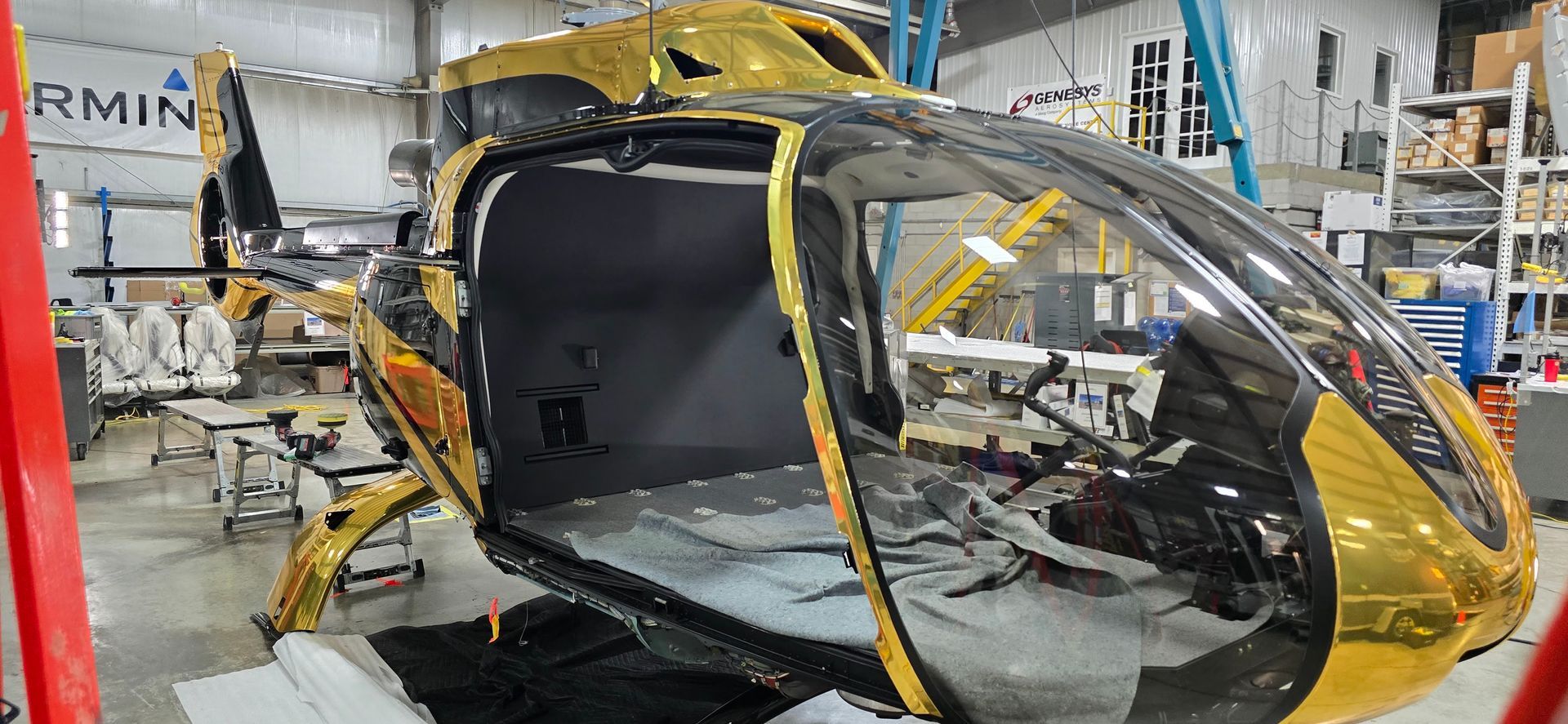 A golden and black helicopter being worked on inside a hangar.