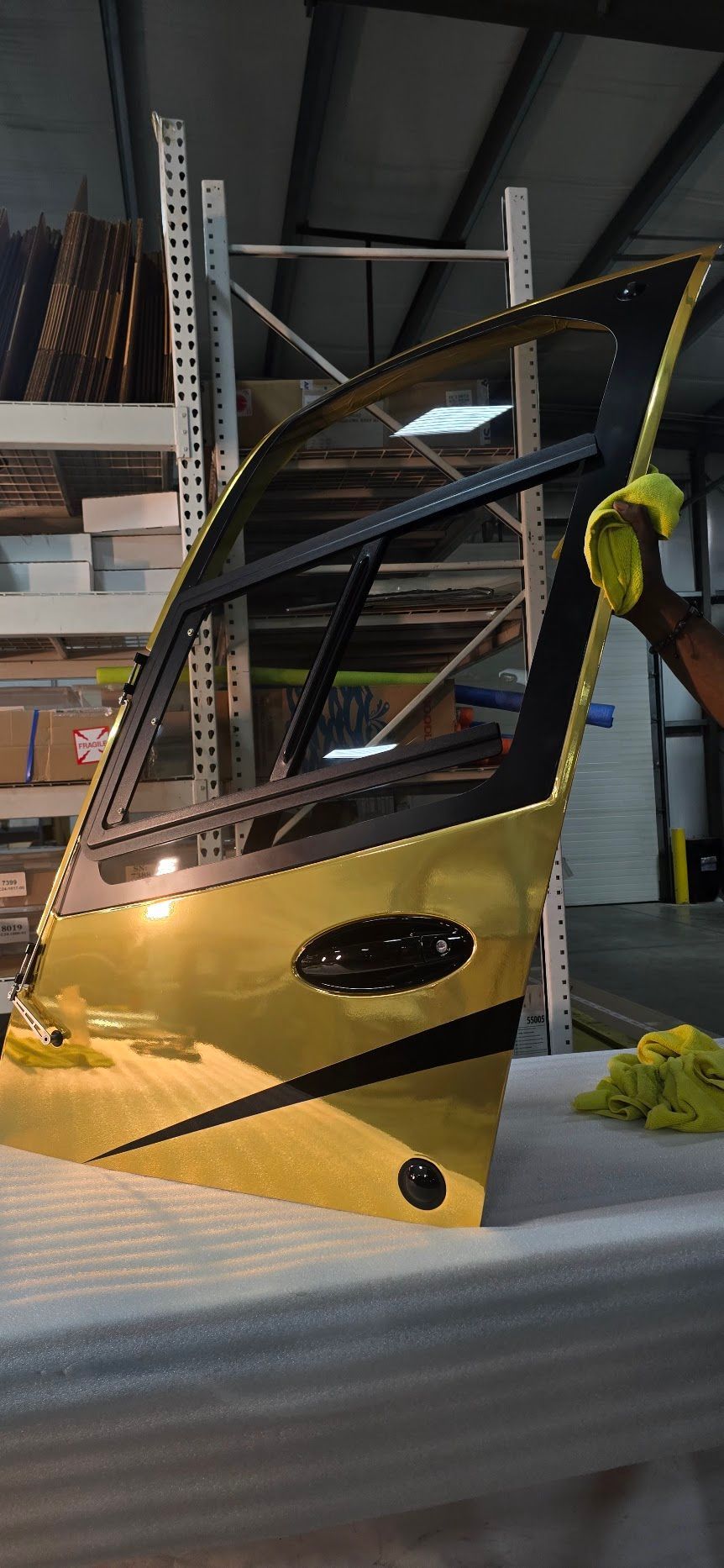 Yellow car door with black accents in a warehouse setting. A person in gloves holds the door.