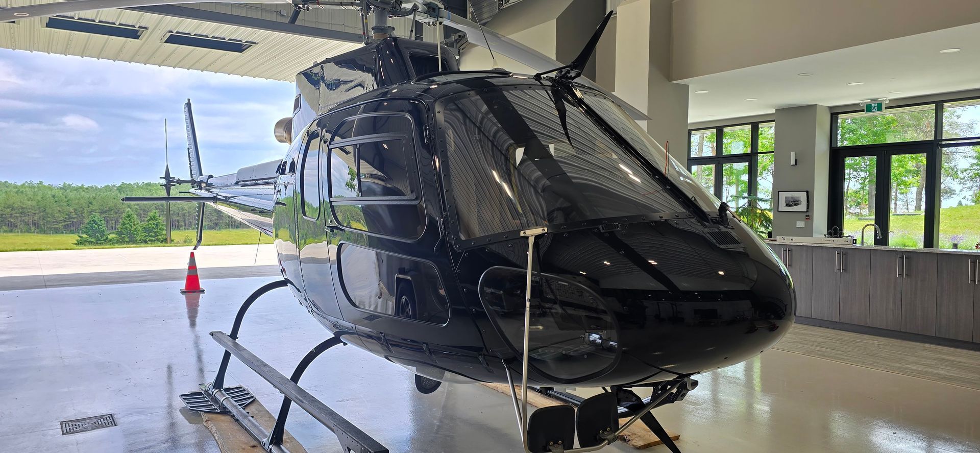 Black helicopter inside a hangar with a glossy finish. It is parked on a paved surface.