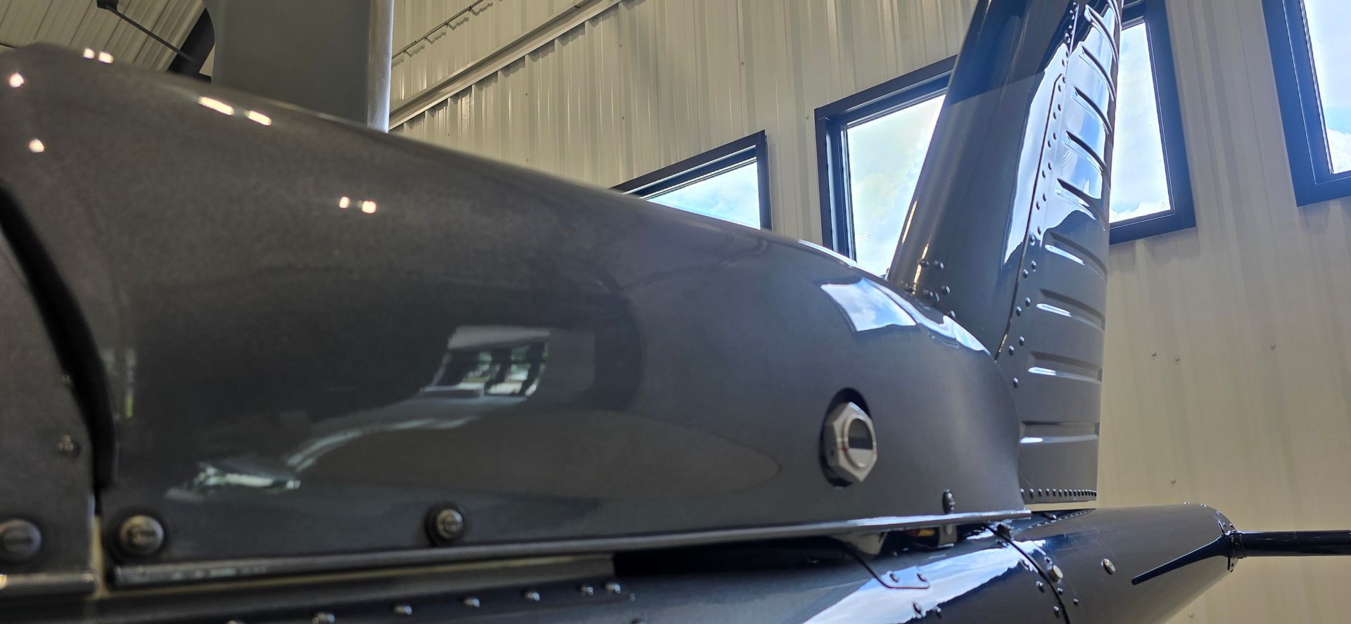 The tail section of a gray helicopter in a hangar with windows.