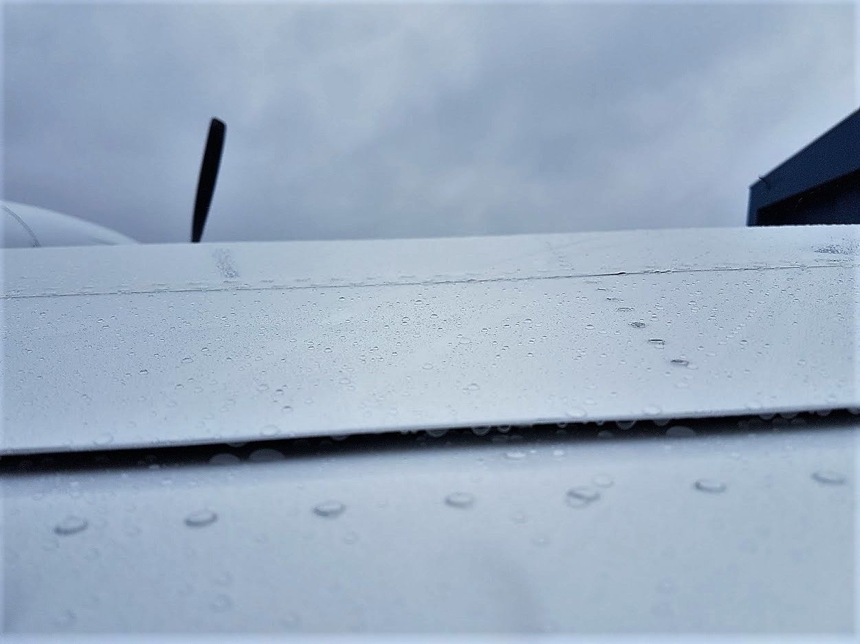 Airplane wing close-up covered in raindrops, cloudy sky background.