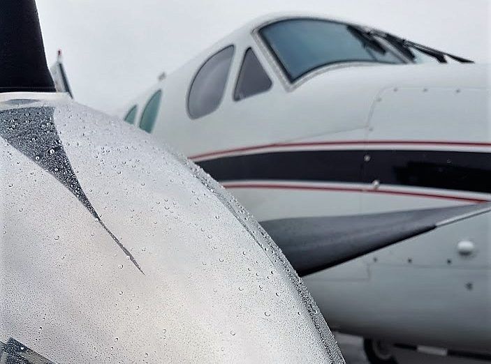 A wet silver airplane propeller with an aircraft in the background.