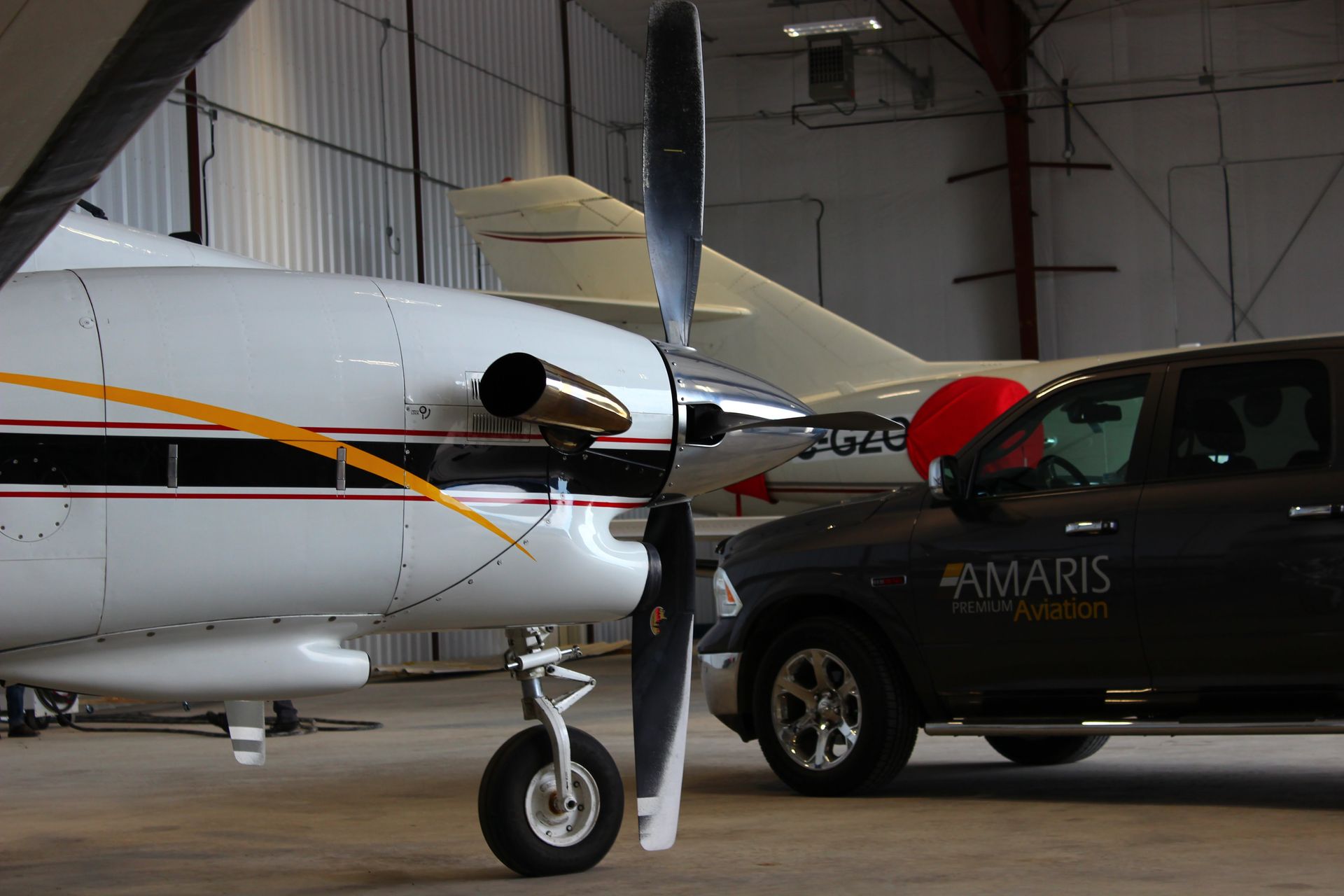 White and gold airplane with a black propeller parked next to a black truck in a hangar.
