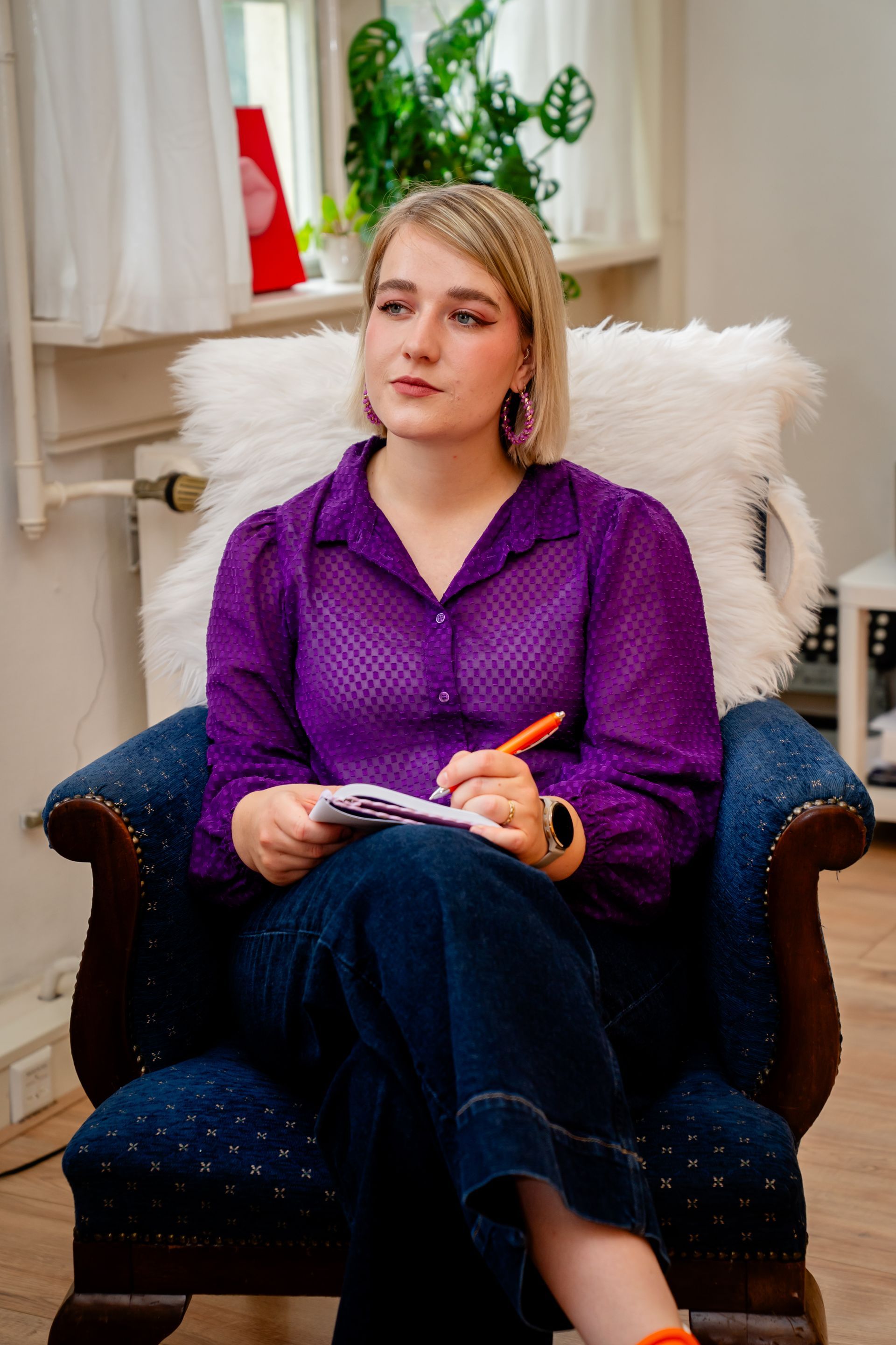 Two people on video call at a wooden table, one drinking from a red straw against an orange wall.