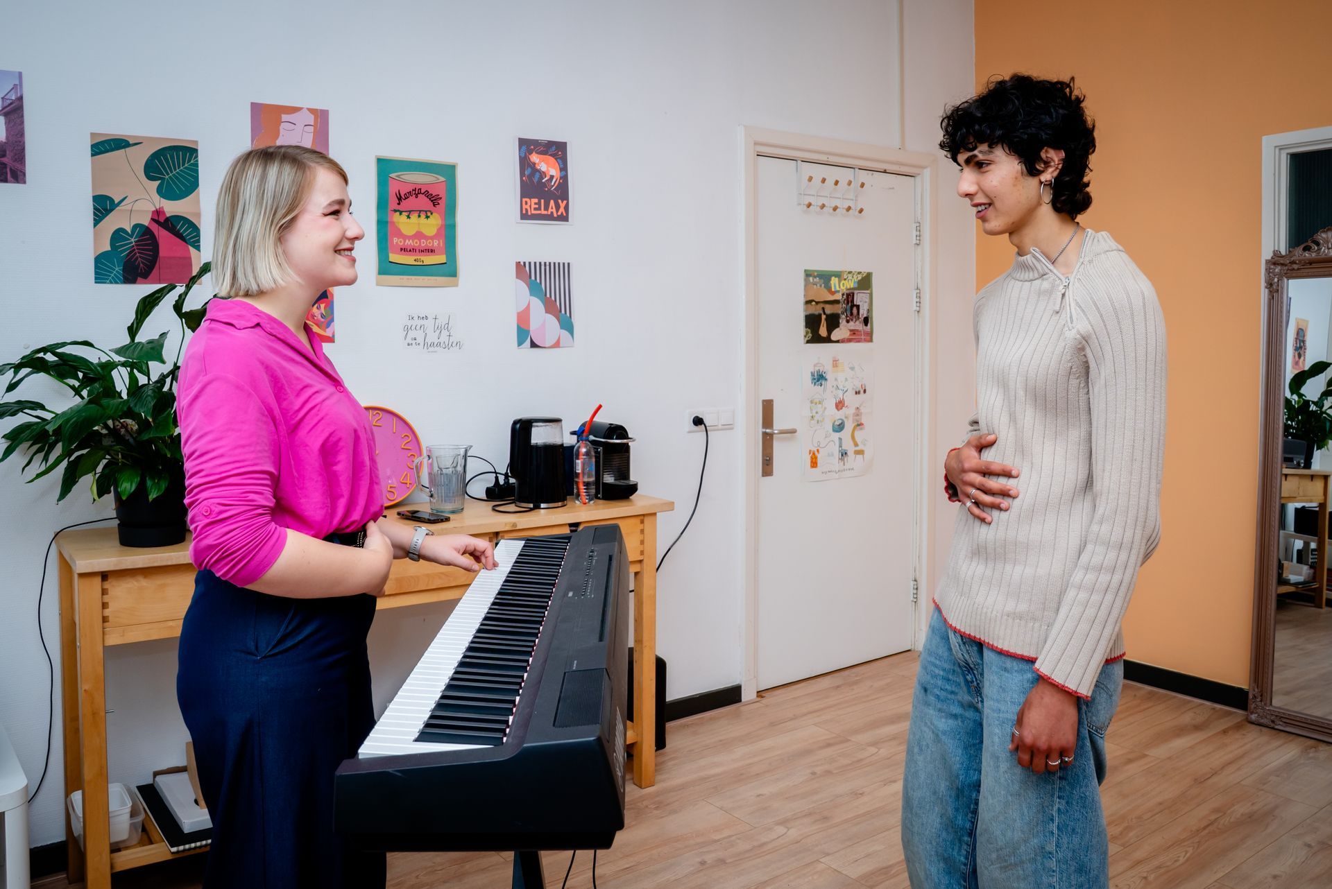 Two people on video call at a wooden table, one drinking from a red straw against an orange wall.