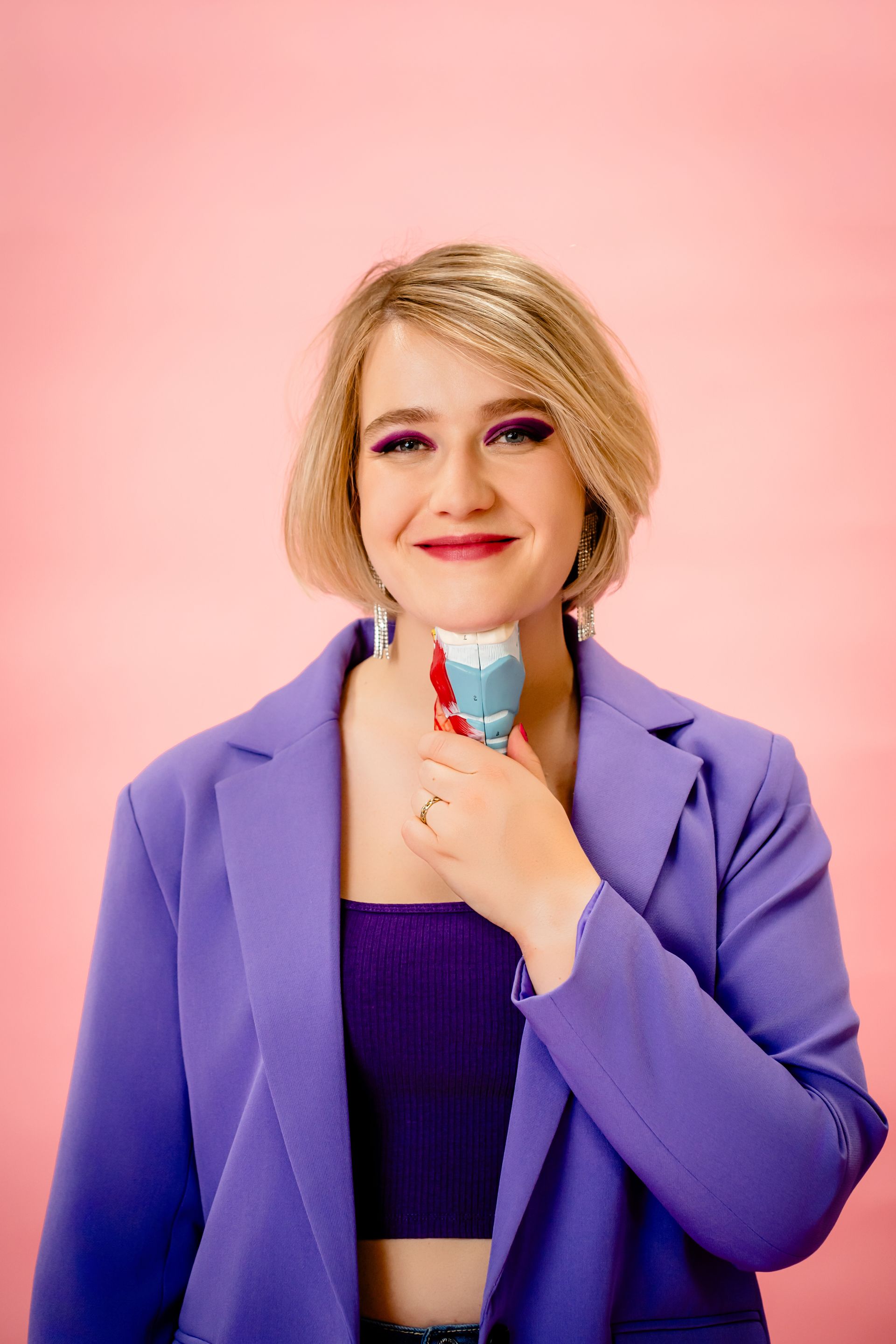 Woman holding a pink wavy mirror, reflecting her smiling image on a magenta background.