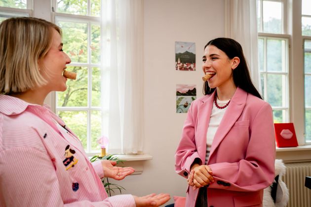 Two women in pink jackets smiling and talking in a bright office with large windows