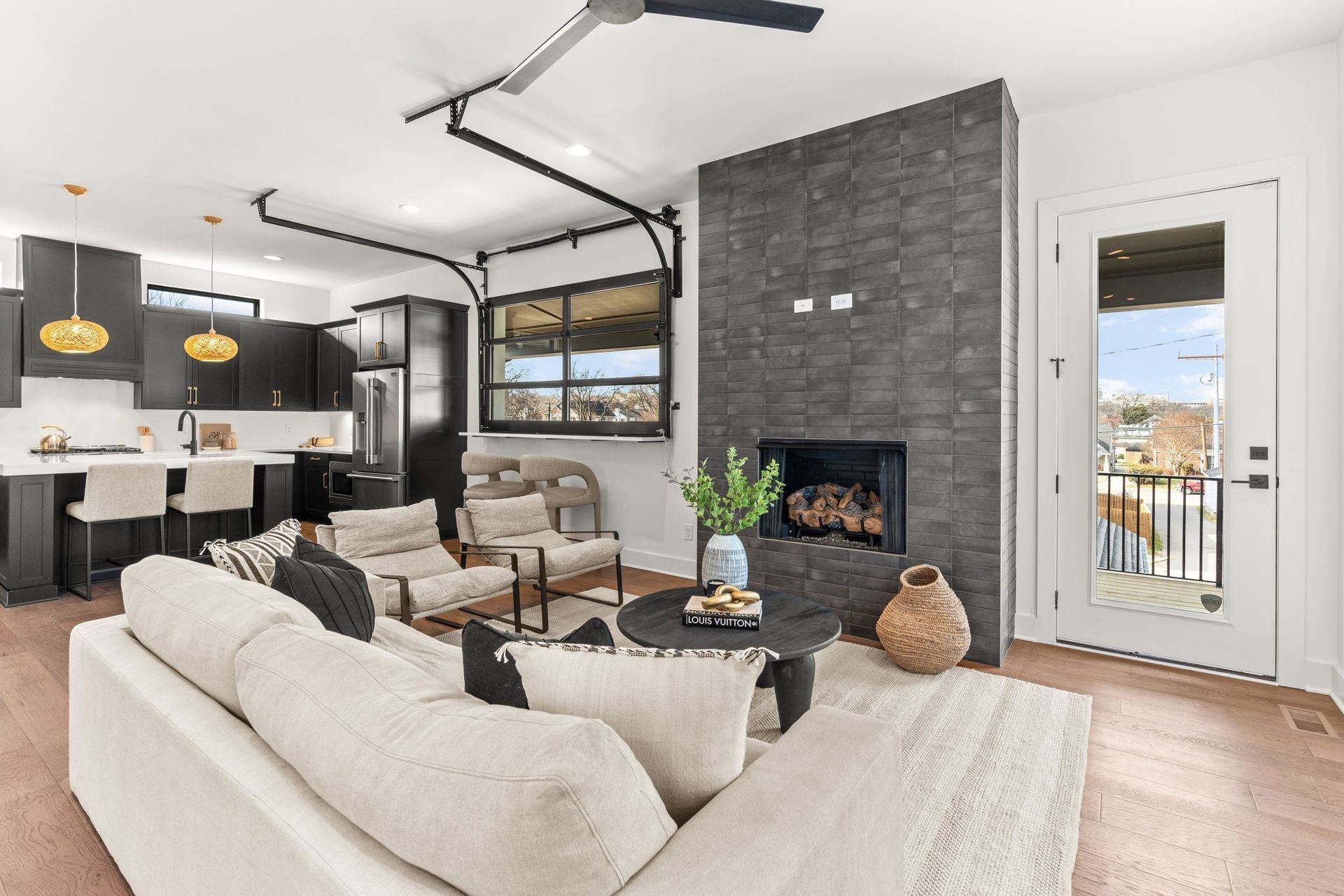 Modern living room with a beige sofa, dark stone fireplace, and open-plan kitchen featuring dark cabinetry.