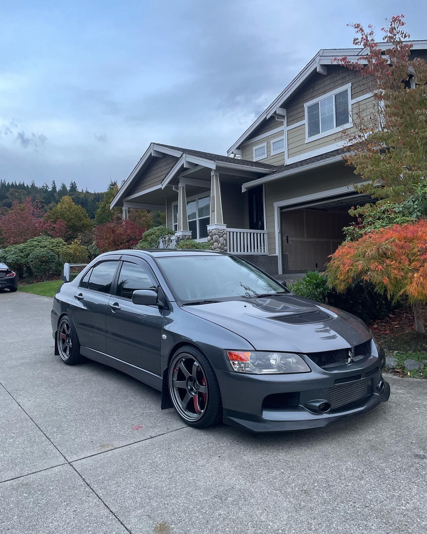Gray Mitsubishi Lancer Evolution parked in front of a house on a driveway; overcast sky.
