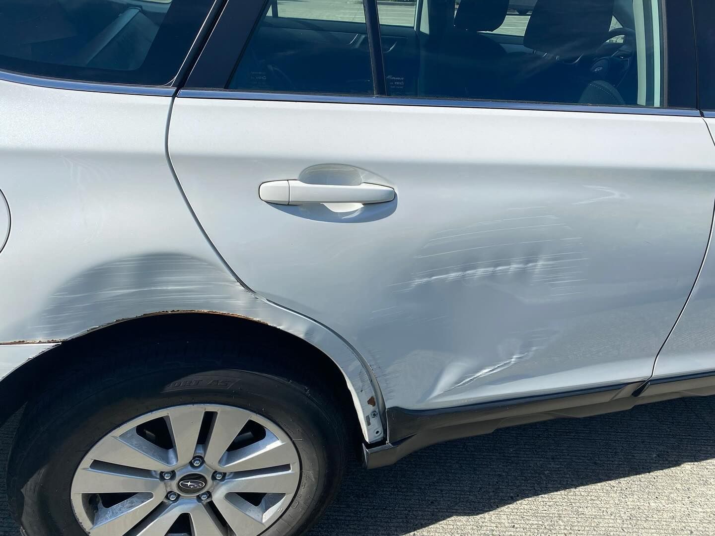 White car with dents and scratches on the rear quarter panel and door.