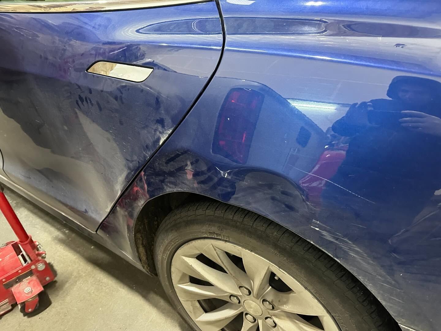Blue car with dented rear door and quarter panel, sitting on a jack.