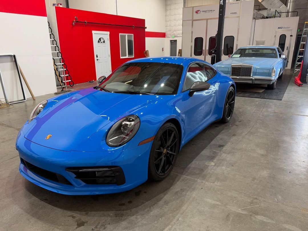 Blue Porsche 911 in a garage, with a light blue classic car in the background.