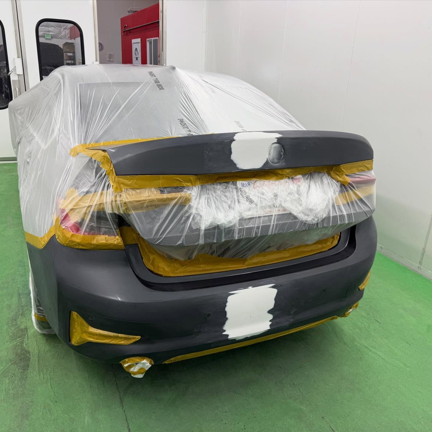 Car rear bumper, covered with plastic wrap and masking tape, prepared for painting in a workshop.