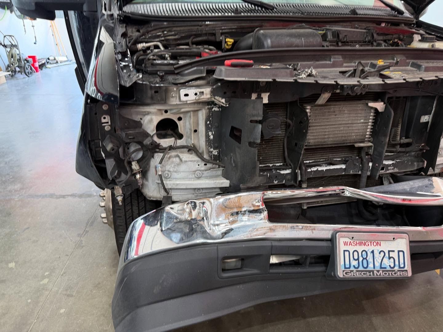 Damaged black pickup truck front end; crumpled bumper, missing hood and panels, exposing engine components.
