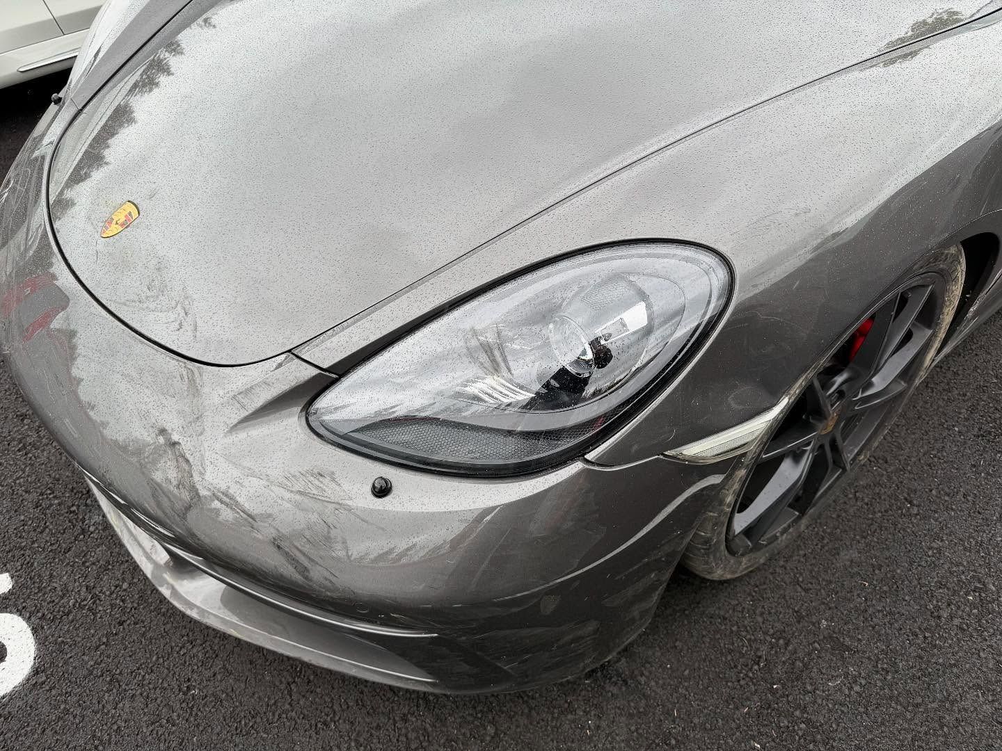 Gray Porsche sports car front detail with headlight, badge, and wheel.