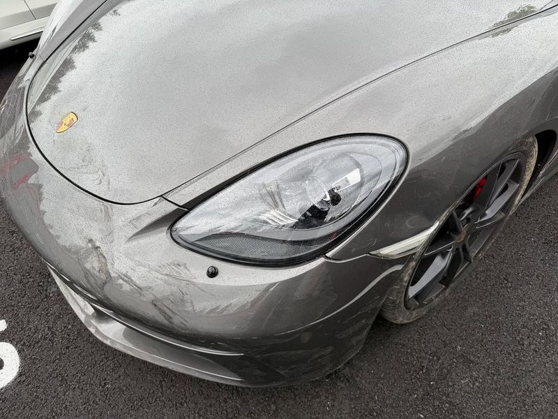 Gray Porsche sports car, close-up of the front end, wet and shiny, parked on asphalt.