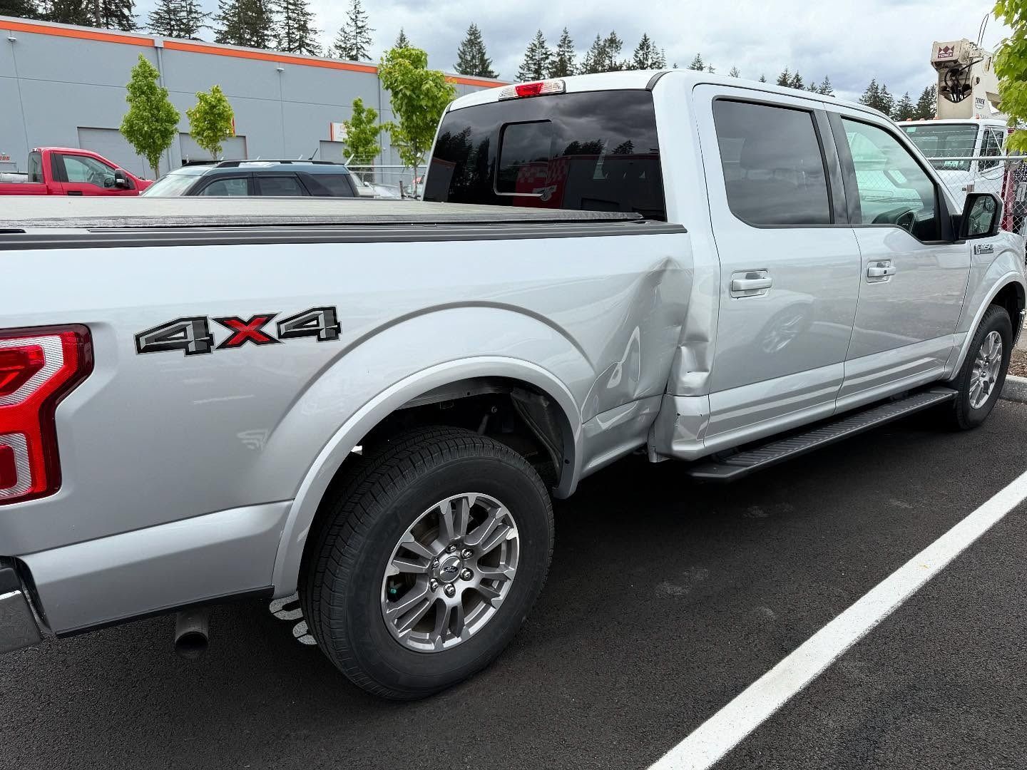 Silver Ford pickup truck with rear side panel damage in a parking lot.