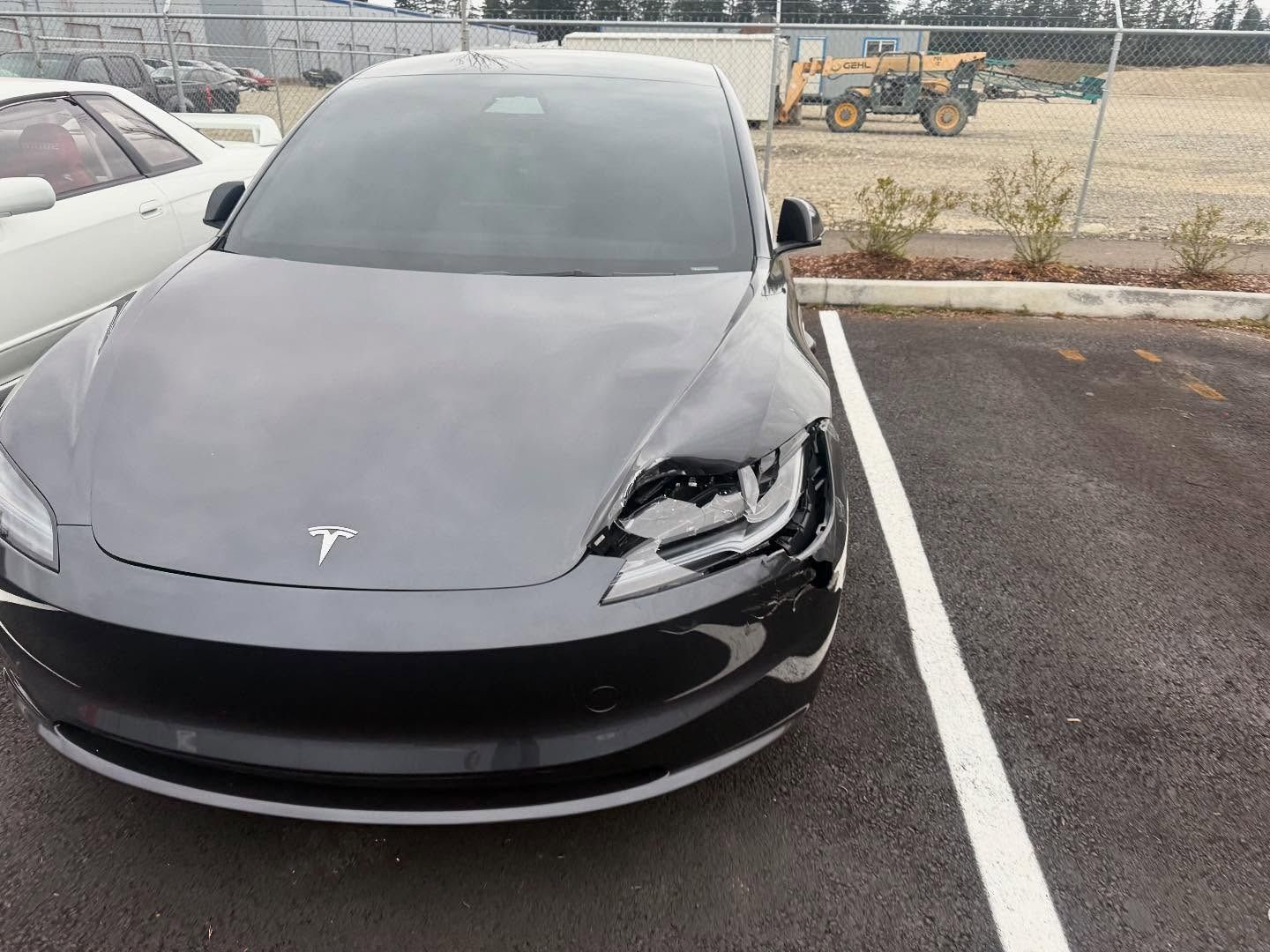 Gray Tesla car parked, with front end damage. Outdoor parking lot setting.