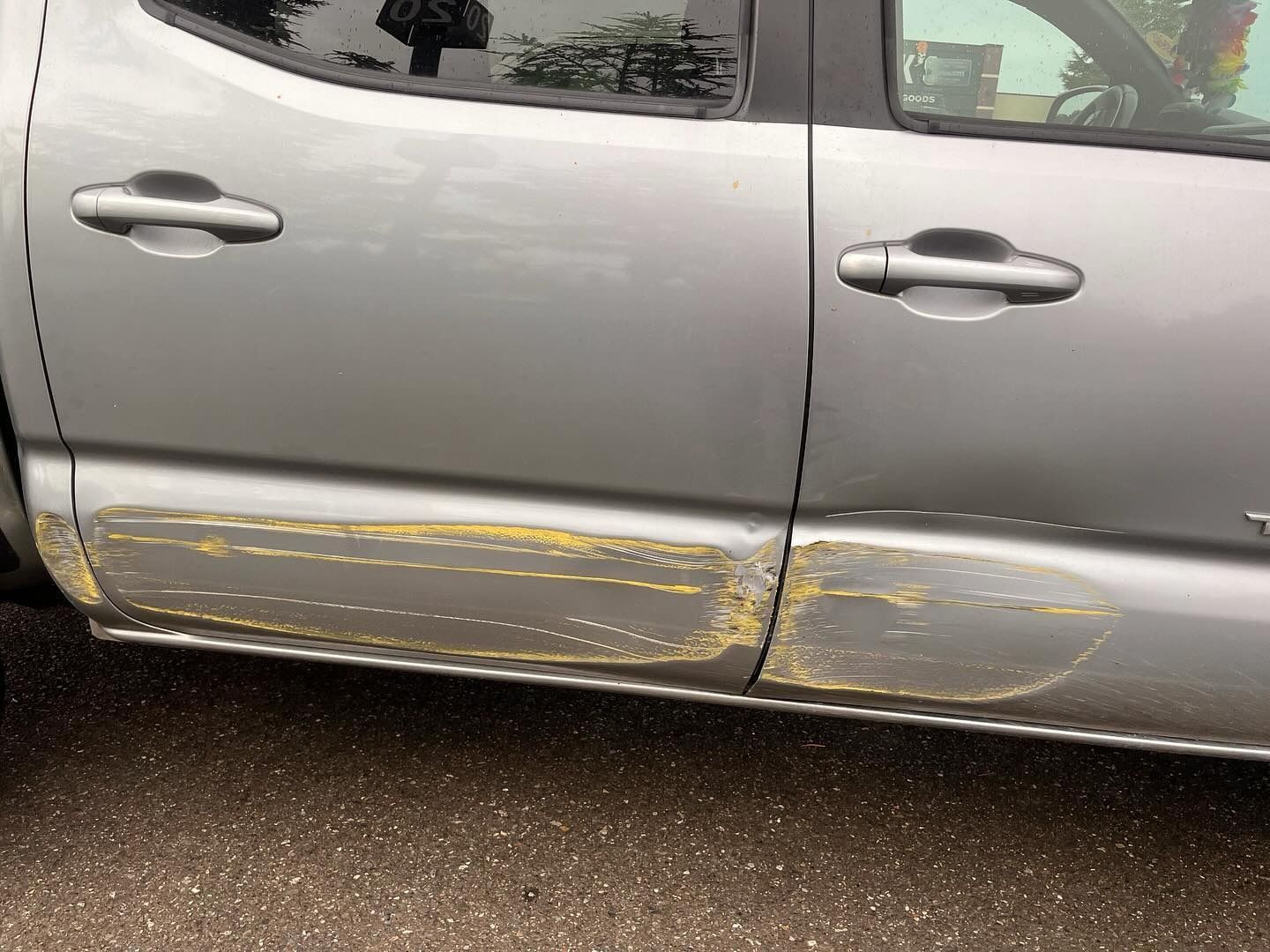 Silver pickup truck with damaged lower door panels, showing yellow undercoat.