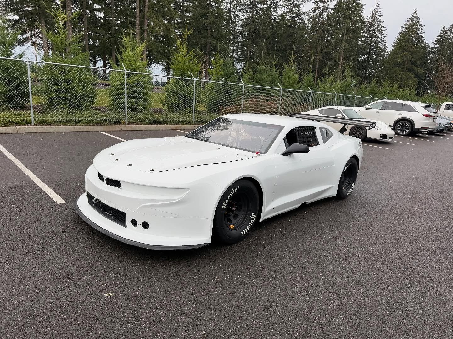 White race car in a parking lot, awaiting a race.