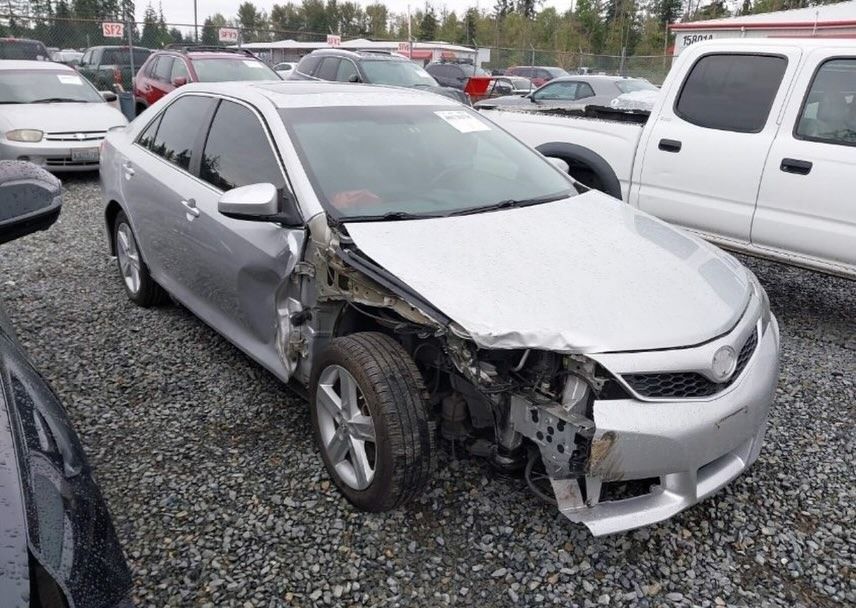 Silver Toyota Camry damaged on the front right side, parked in a lot with other vehicles.