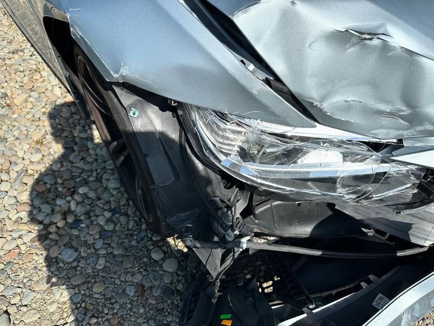 Damaged silver car front end; crumpled hood, broken headlight, exposed components.