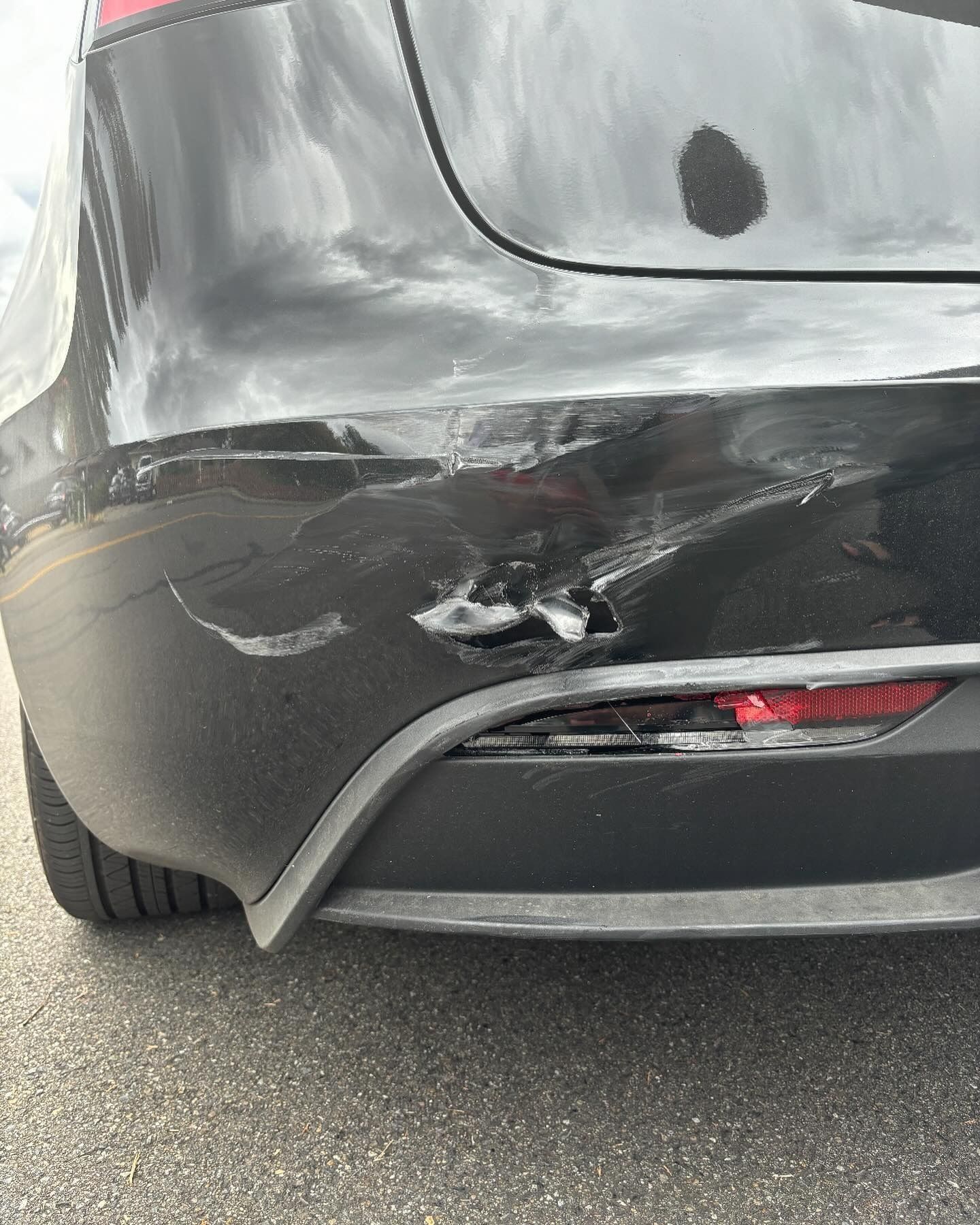 Damaged black Tesla rear bumper. White scrape marks and dent near taillight.
