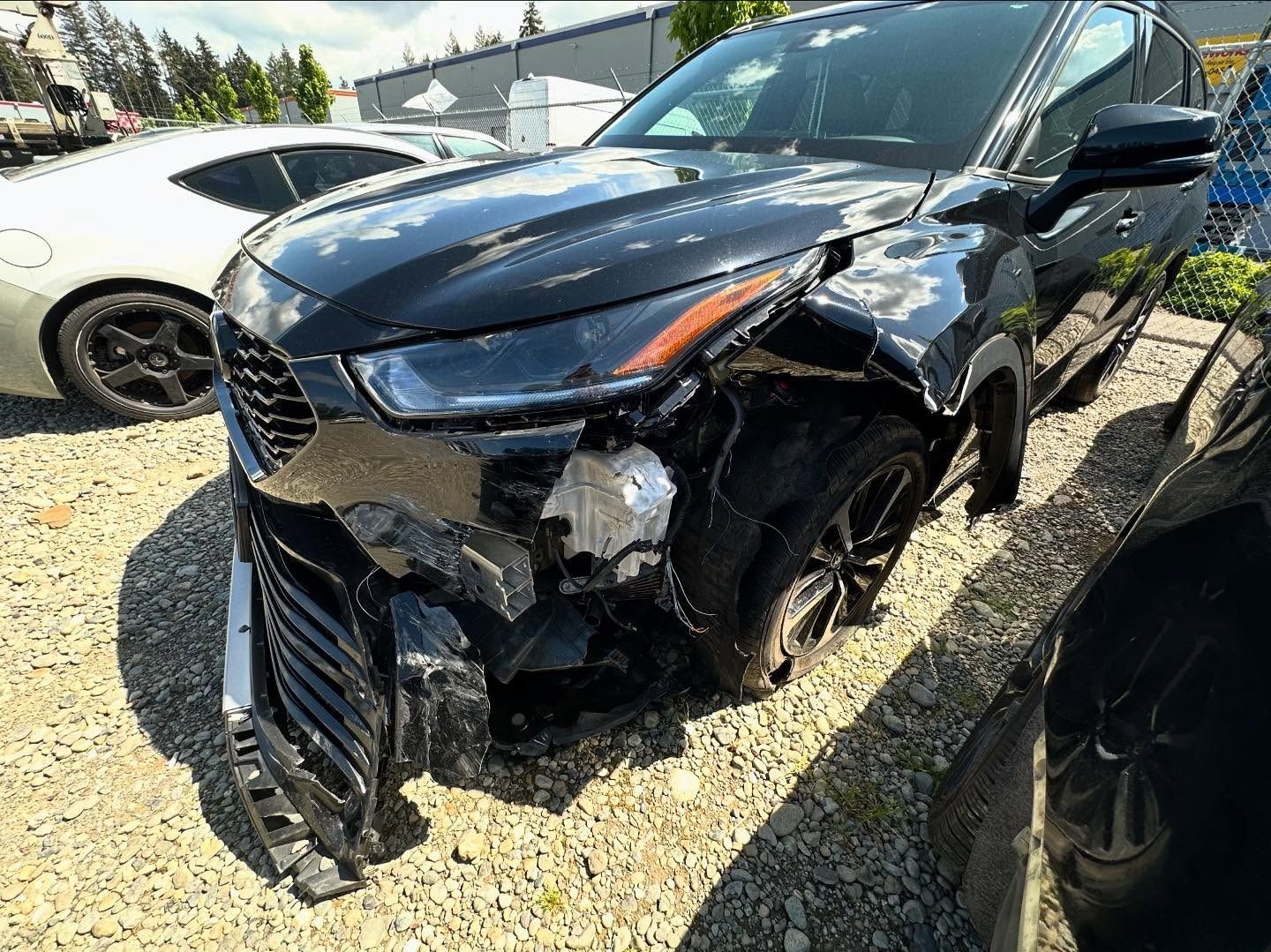 Black SUV with extensive front-end damage; parked outdoors on gravel.