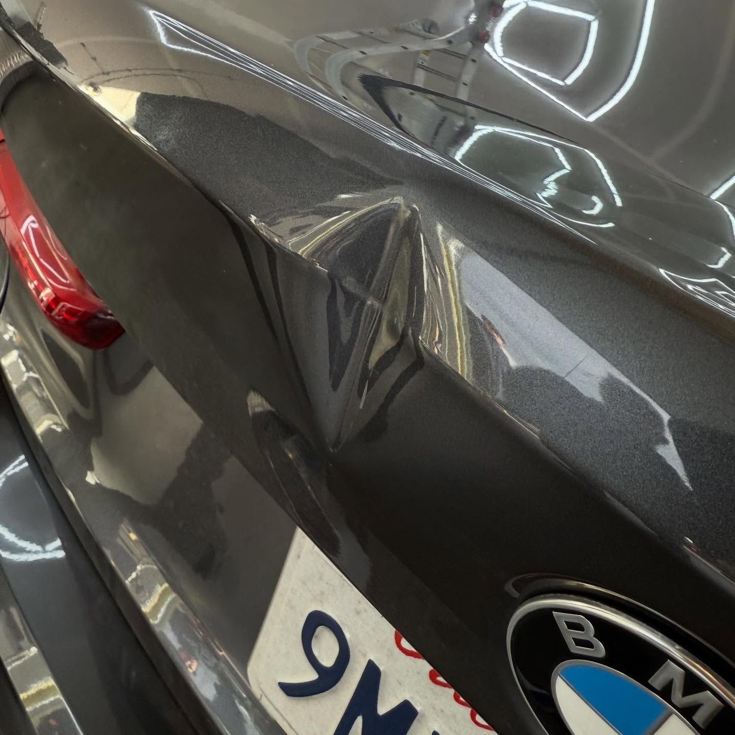 Gray BMW car with dented rear quarter panel.