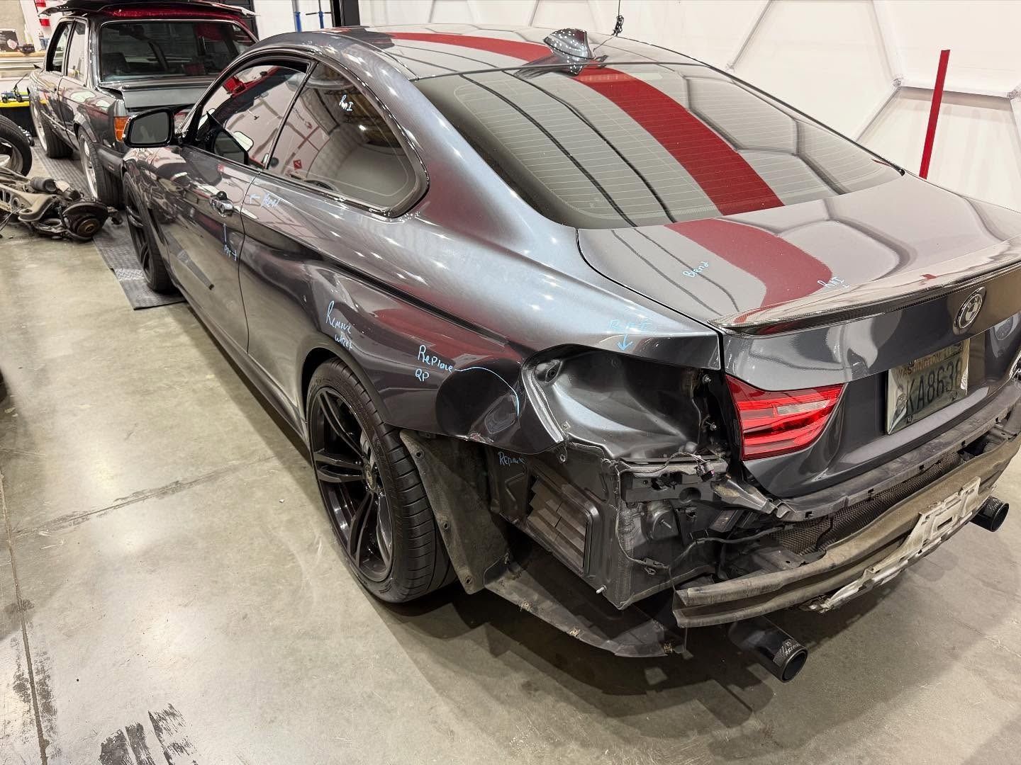Damaged gray BMW coupe in a repair shop, rear end collision.