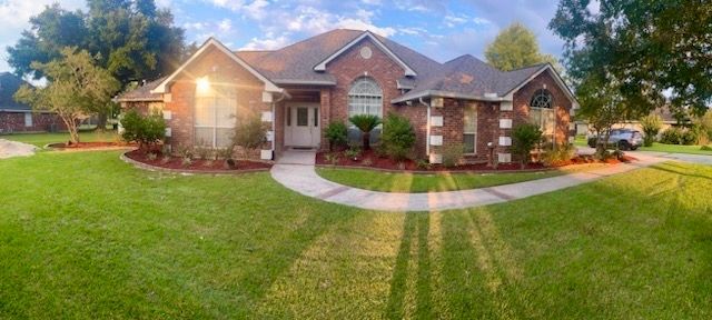 Brick suburban house with a manicured lawn, front walkway, and sunlit trees
