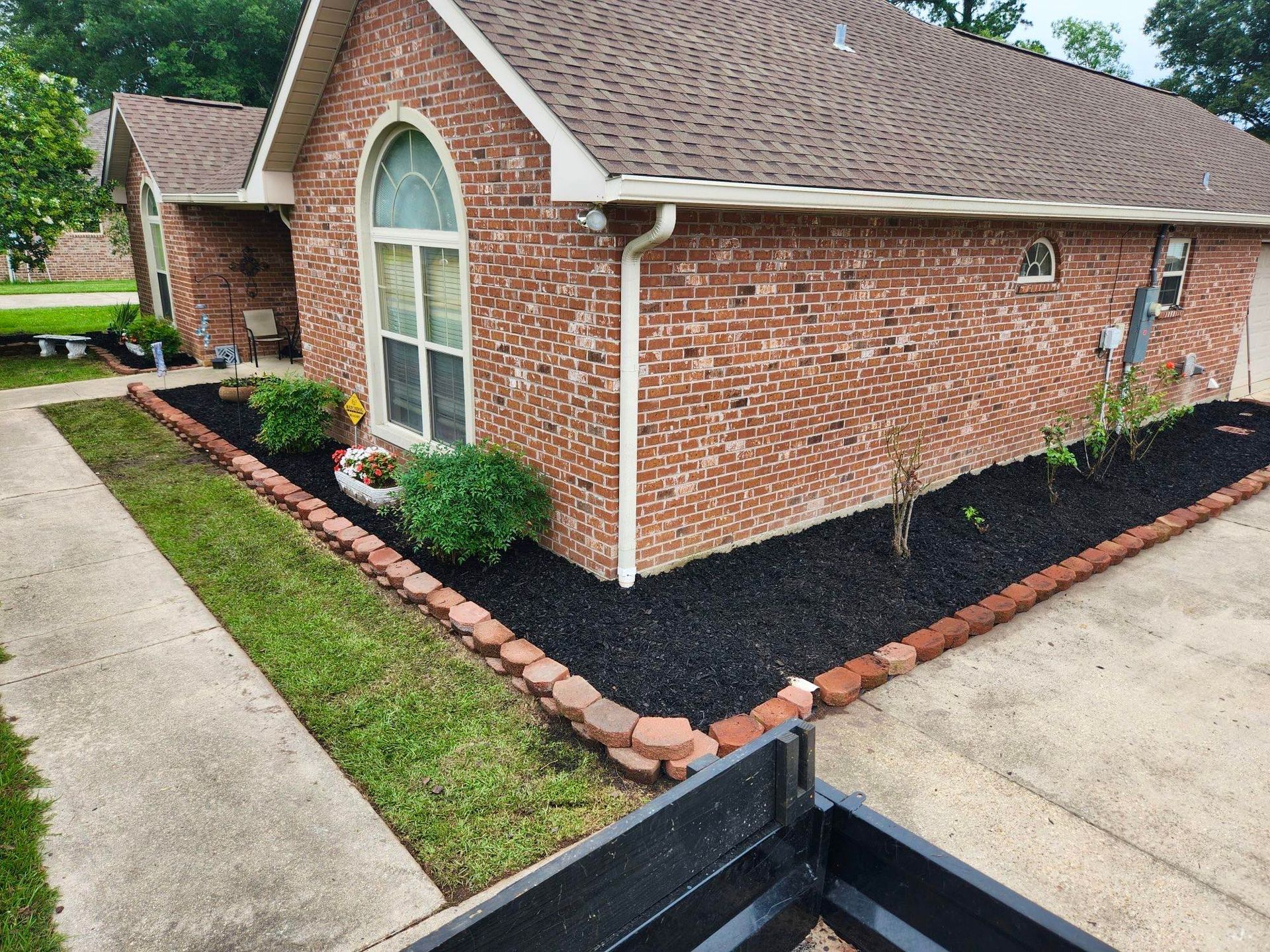 Brick house with arched window, landscaped mulch beds, and a concrete driveway.