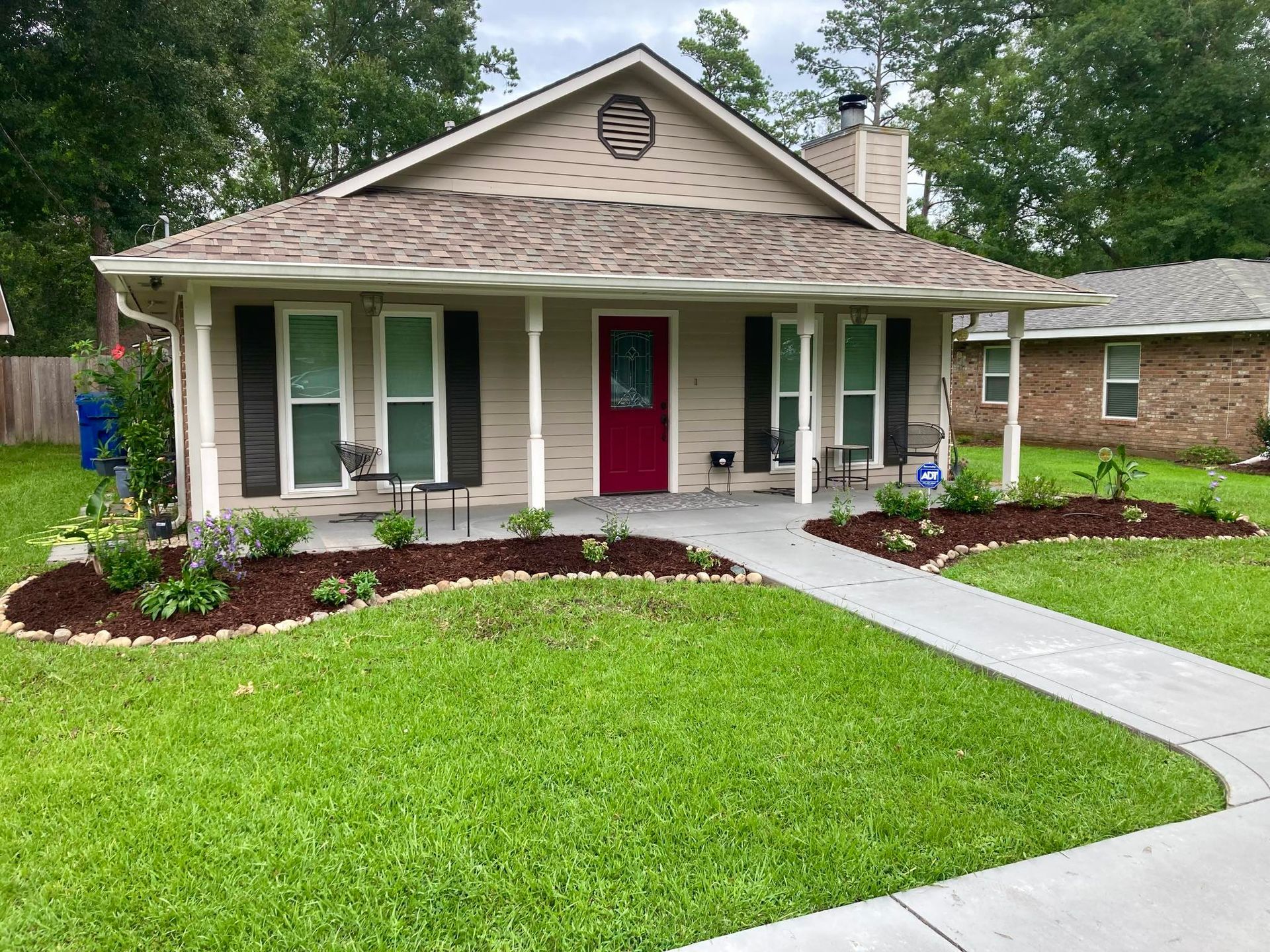 Single-story house with a red front door, green shutters, white porch, and a curved walkway.