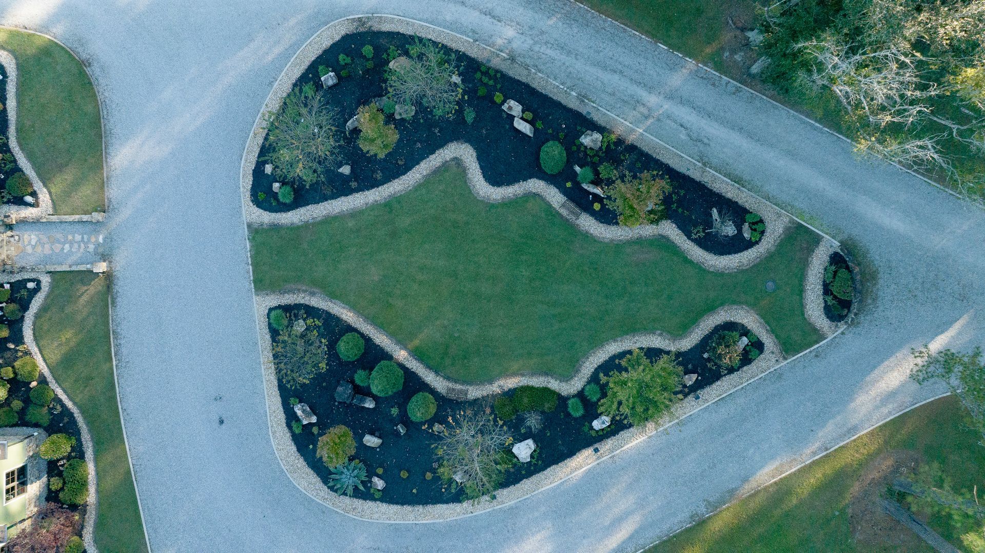 Aerial view of a landscaped island with winding paths, grass, and a gravel driveway.