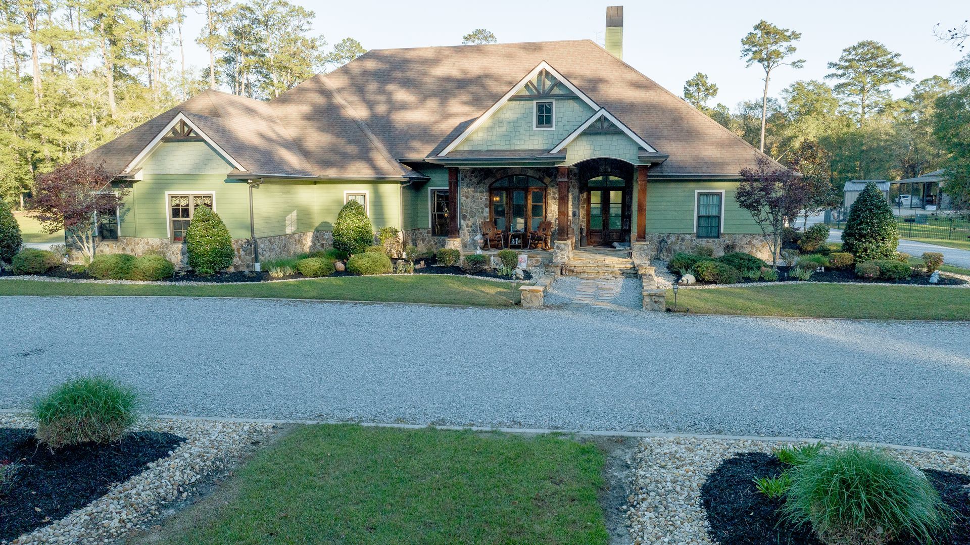 Single-story house with a front porch, gravel drive, and landscaped yard in daylight