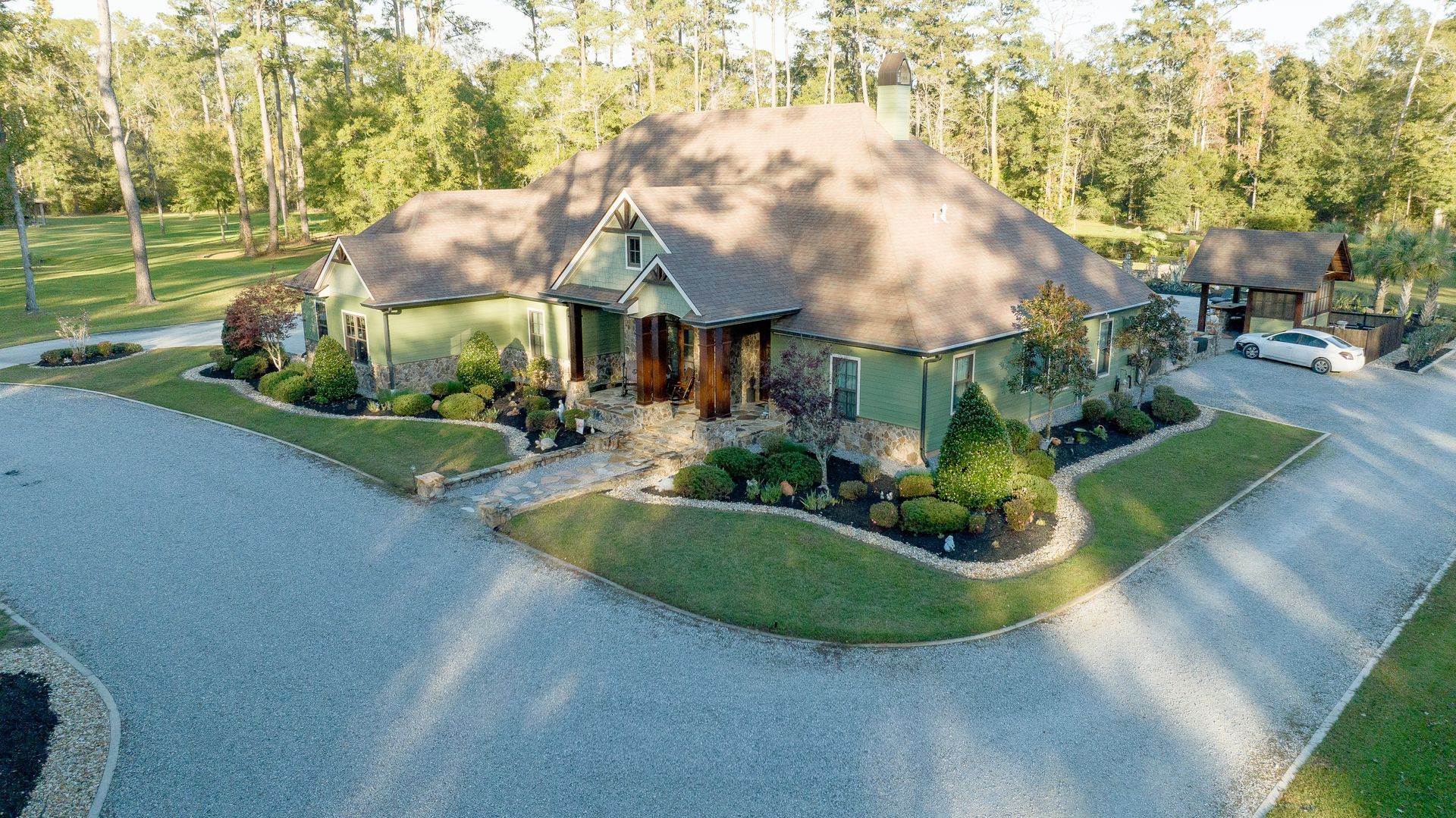 Aerial view of a house with landscaped garden and curved gravel driveway in a wooded area