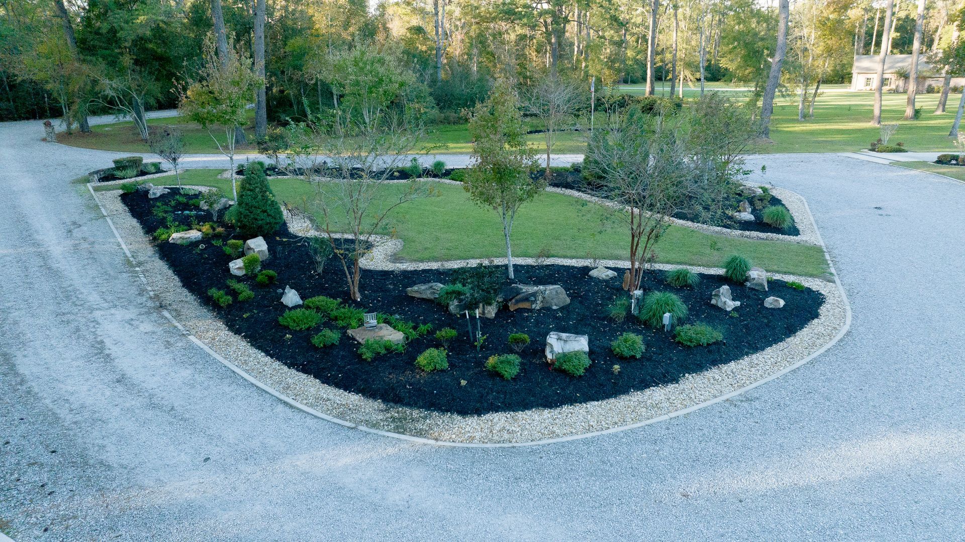 Curved gravel driveway around a landscaped garden bed with young trees and shrubs