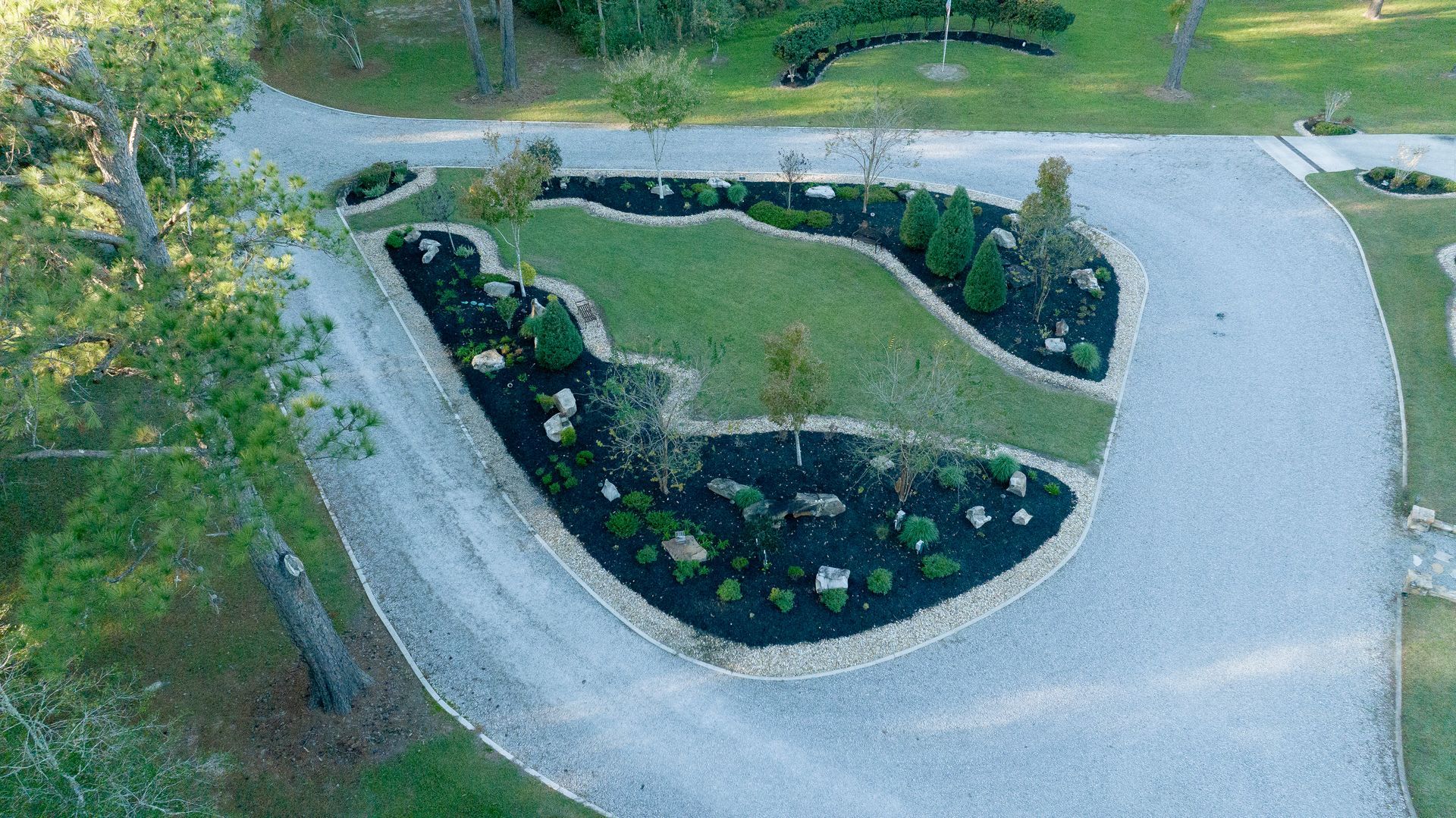 Aerial view of a landscaped garden bed with curved pathways and white flowers beside a driveway.